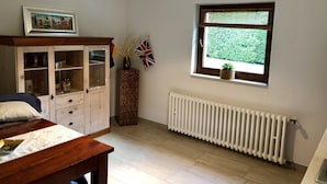 Ein Schlafzimmer mit Bett, einem Holzkapfenständer, einer Heizung und einem Fenster mit Blick auf Grünflächen.