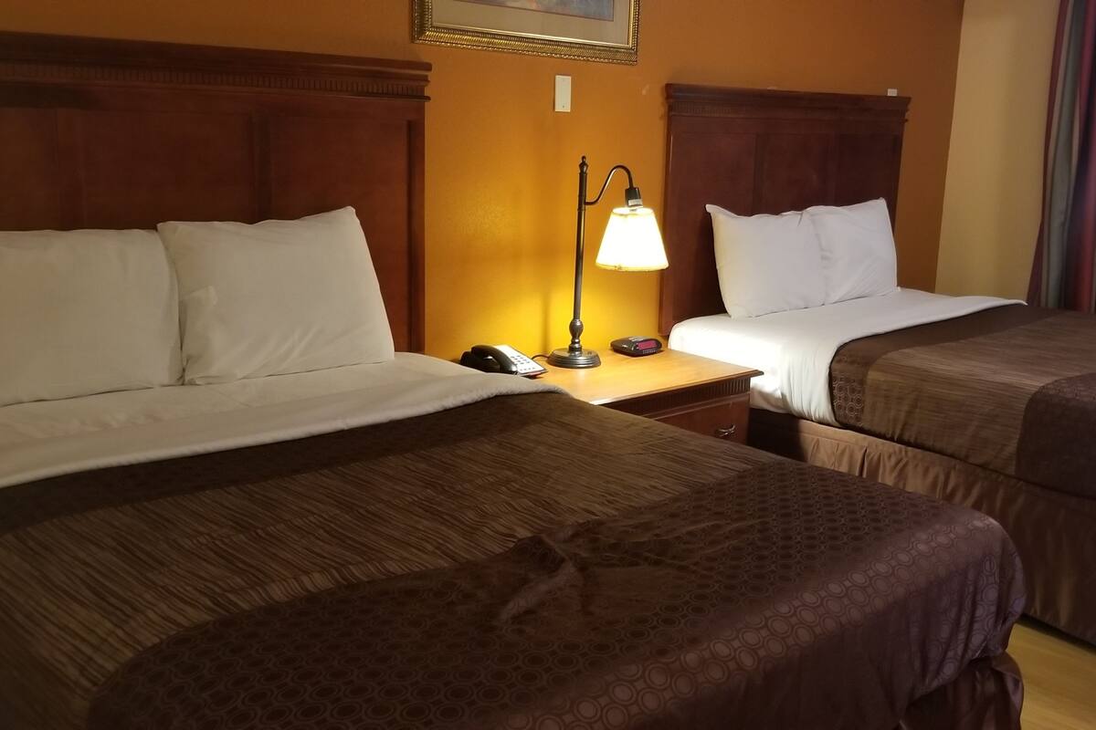 A hotel room with two beds, a nightstand with a lamp, and a window with curtains.