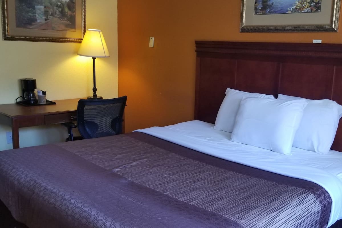 A hotel room with a bed, a desk with a lamp, and a phone on a side table.