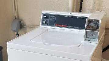 A white commercial washer with a control panel, located on a concrete floor next to a beige wall and a red cloth.
