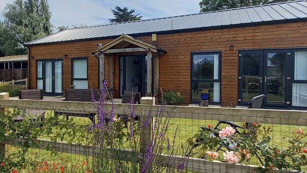 Una casa di legno a due piani con un portico, ampie finestre e un giardino recintato con diverse piante e fiori.