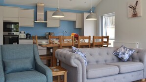 Una cucina moderna con mobili bianchi, un tavolo da pranzo con sedie e un divano grigio con cuscini decorati.
