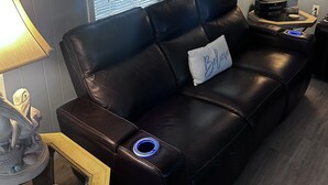 A modern living room with a black leather sofa, a side table with a lamp, and a decorative plant. - Welcome to our Beach House ! We have recently totally renovated and refreshed. (Port Orange)