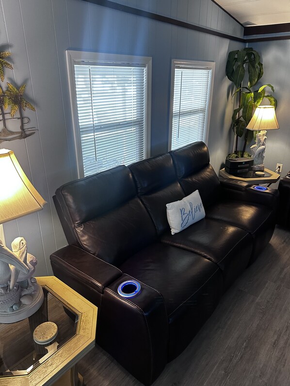 A modern living room with a black leather sofa, a side table with a lamp, and a decorative plant.
