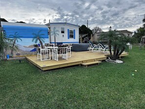 A deck with outdoor furniture, a small building, and a grassy area. - Welcome to our Beach House ! We have recently totally renovated and refreshed. (Port Orange)