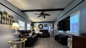 A living room with a ceiling fan, a sofa, a coffee table, a TV, and a fireplace. - Welcome to our Beach House ! We have recently totally renovated and refreshed. (Port Orange)
