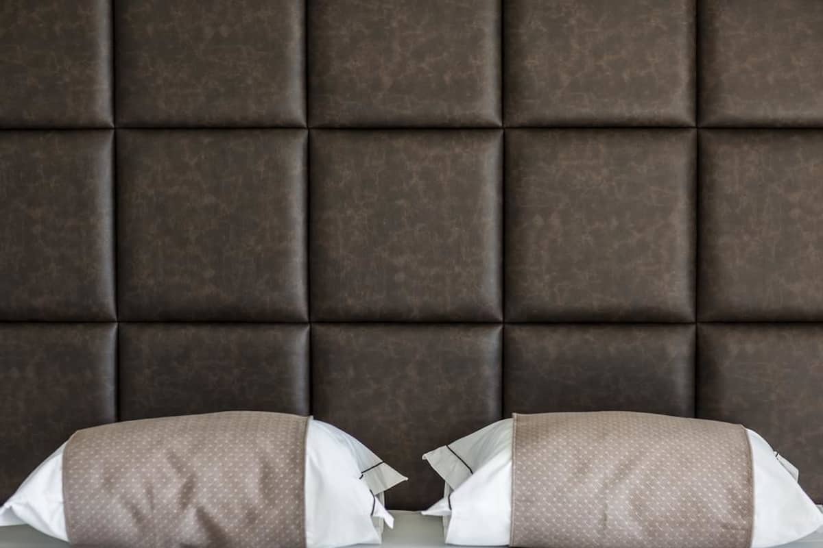 A room with a dark brown padded headboard and two pillows with a white and brown pattern.