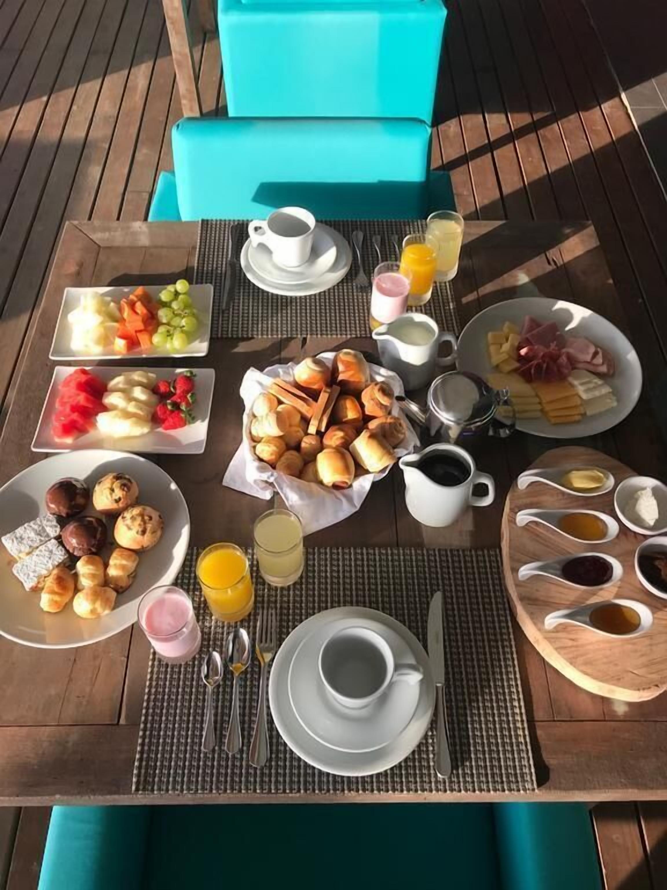 Una mesa de madera con platos de frutas, pasteles y bebidas para el desayuno.