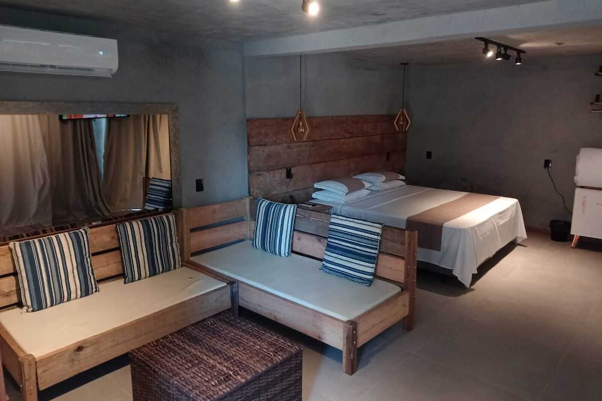 A room with a sofa, two beds, a wooden headboard, a small table, and a wall-mounted air conditioner.