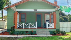 Ein grünes Haus mit Veranda, Eingangstür und kleinem Vorgarten.
