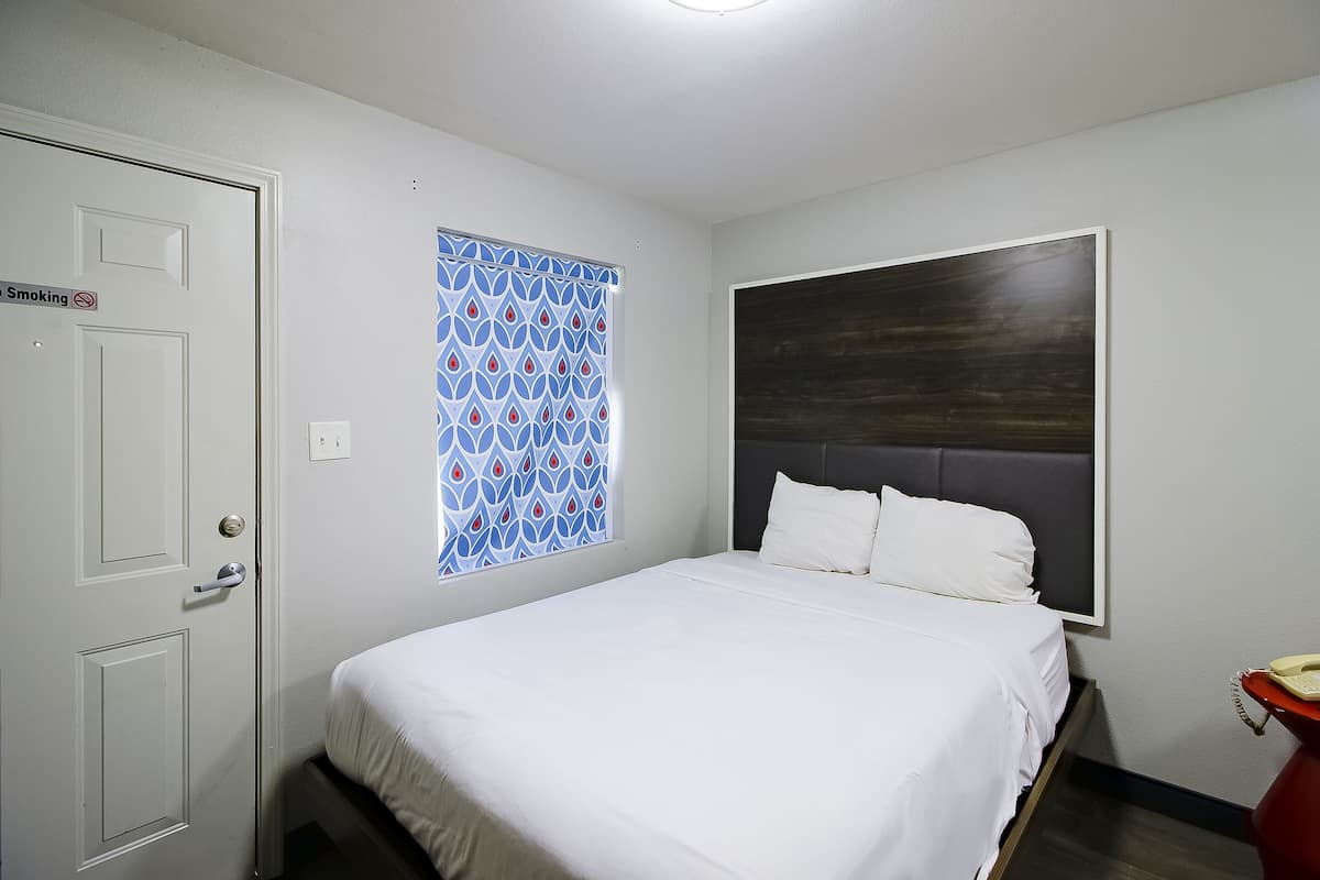 Een hotelkamer met een bed, een raam met een blauw patroon gordijn, een bedtelefoon en een deur met een ‘Niet roken’-bord.