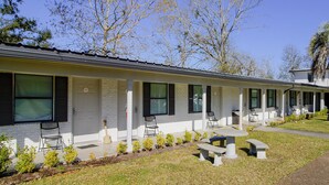 A motel with a row of rooms, a covered patio, and a small lawn area with benches.