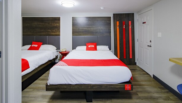 A hotel room with two beds, each with red and white bedding, a wooden headboard, and a bedside table with a lamp.