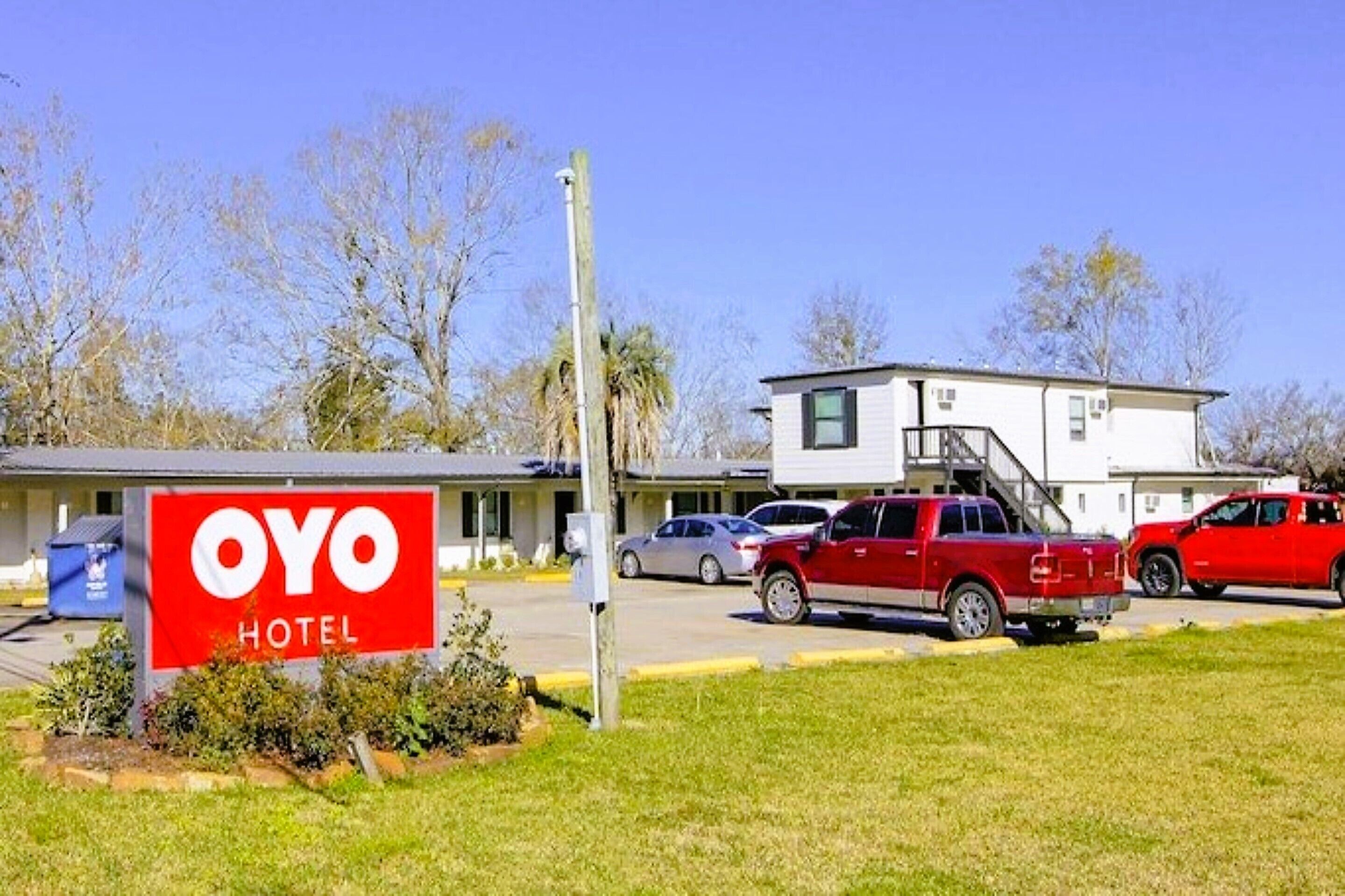 A hotel named OYO with a signboard, a parking area with several cars, and a building with a staircase.