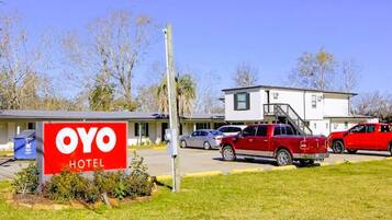 A hotel named OYO with a signboard, a parking area with several cars, and a building with a staircase.