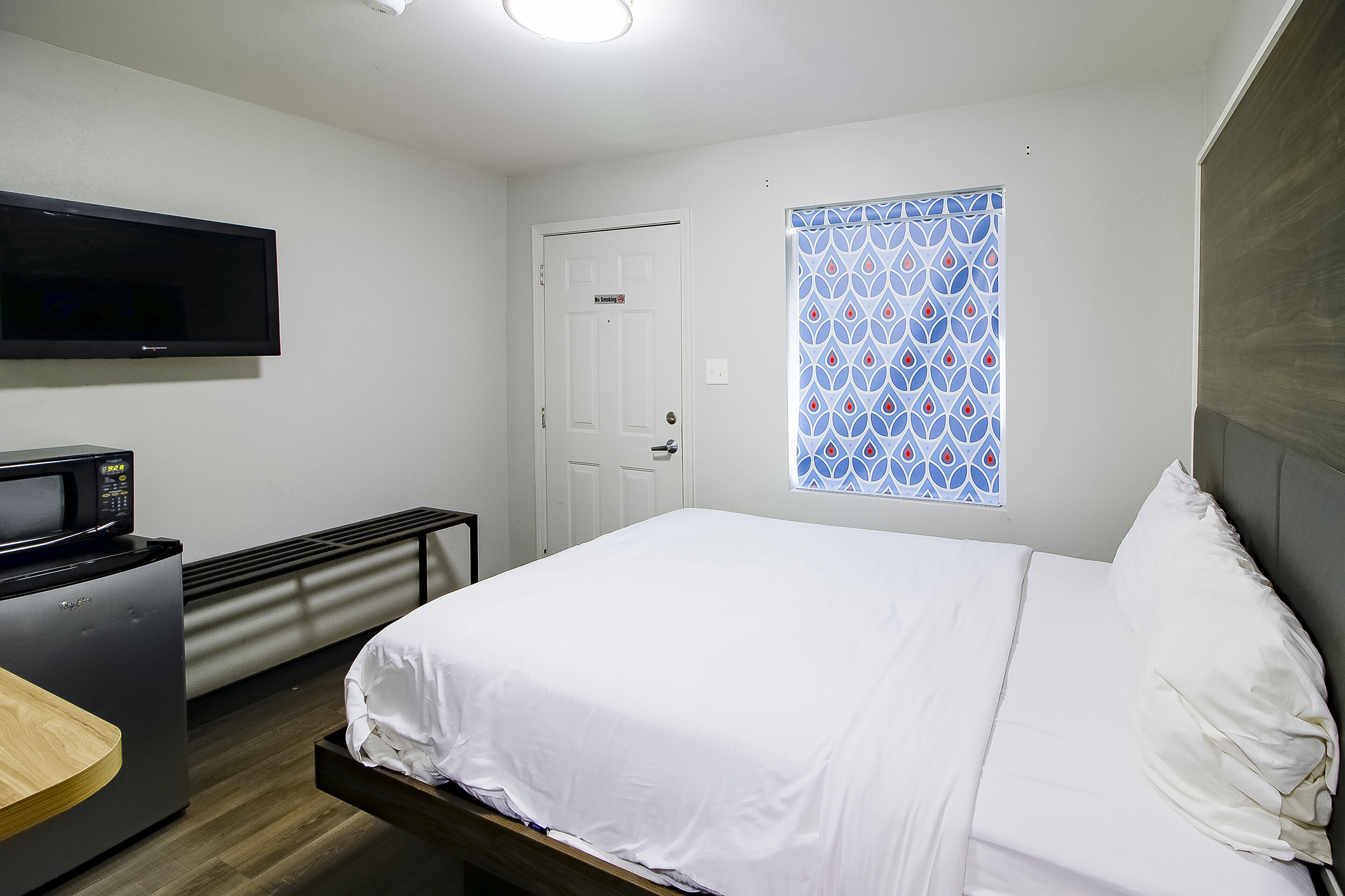 Habitación de hotel con cama, televisión, microondas y escritorio pequeño.