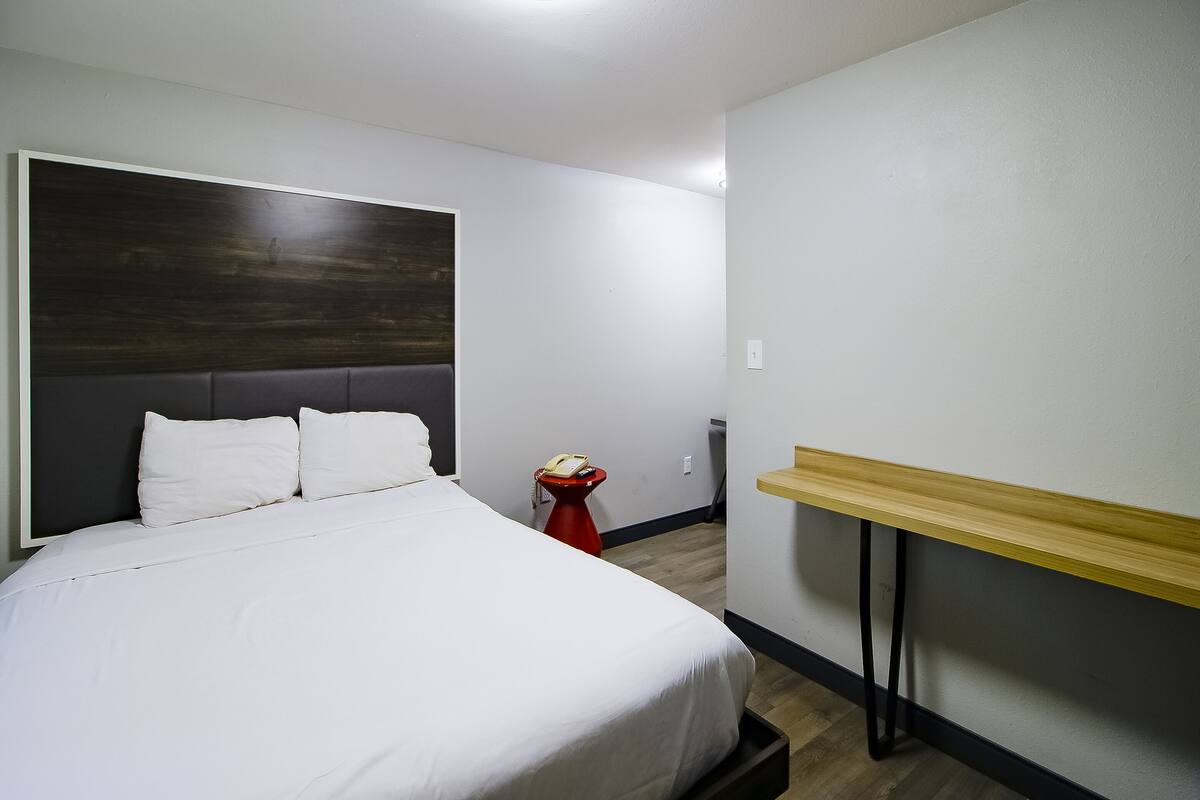 Een hotelkamer met een groot bed, een houten hoofdeinde, een rode nachtkastje met een telefoon en een houten plank.