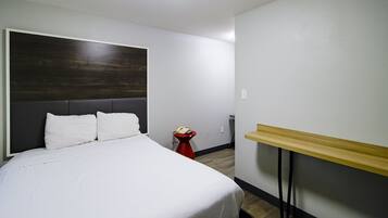 A hotel room with a large bed, a wooden headboard, a red side table with a telephone, and a wooden shelf.