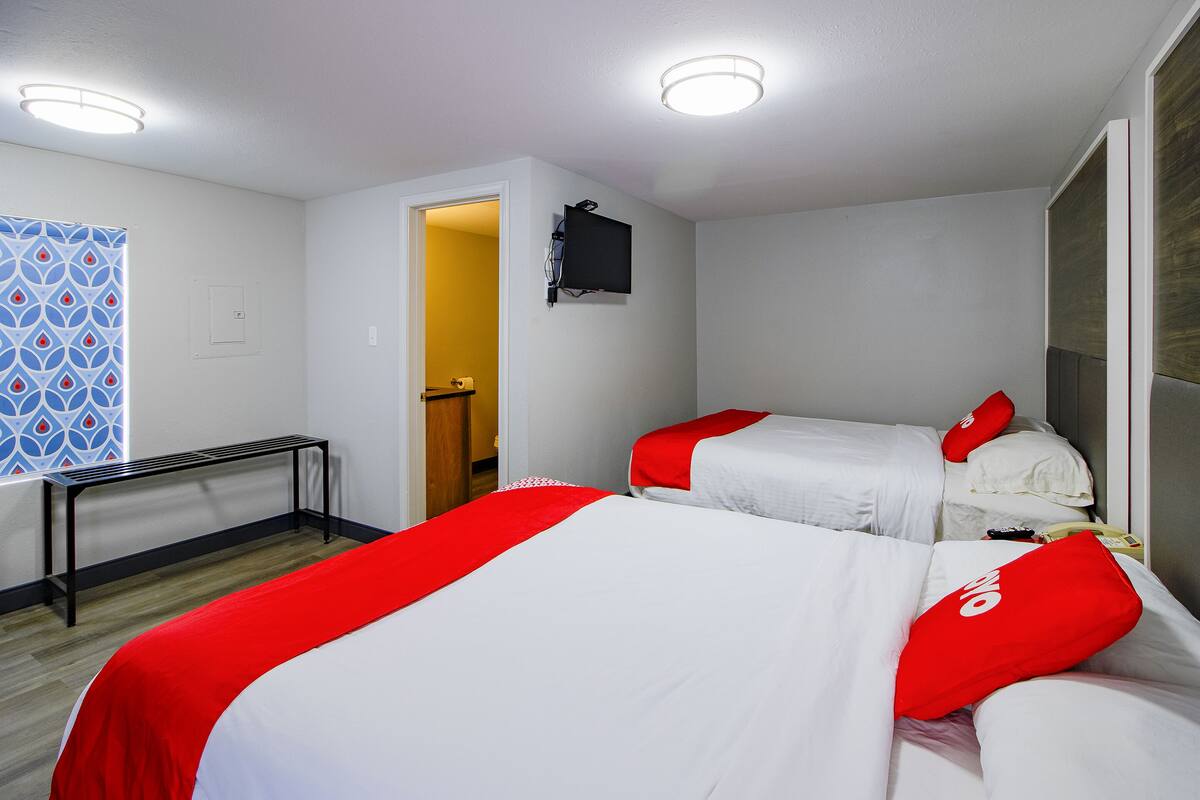 Een hotelkamer met twee bedden, elk met rode en witte beddengoed, een flatscreen televisie aan de wand en een klein bureau met een stoel.