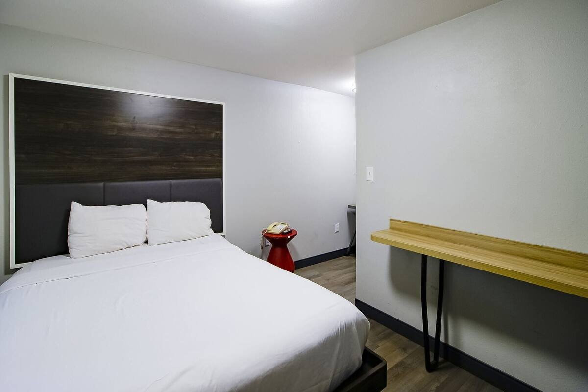 Een hotelkamer met een bed, een nachtkastje, een rode telefoon en een houten bank.