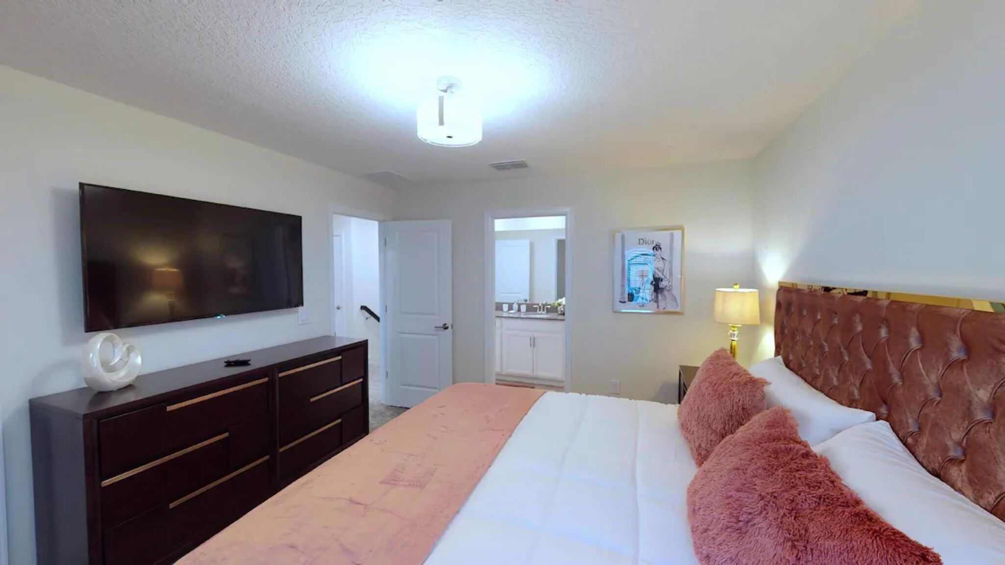 Un dormitorio con una cama, un televisor, un aparador, un espejo y una puerta que da a un baño.