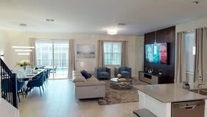 Una sala moderna con un sofá, sillones, una mesa de centro y un televisor. Hay un comedor con sillas y una mesa.