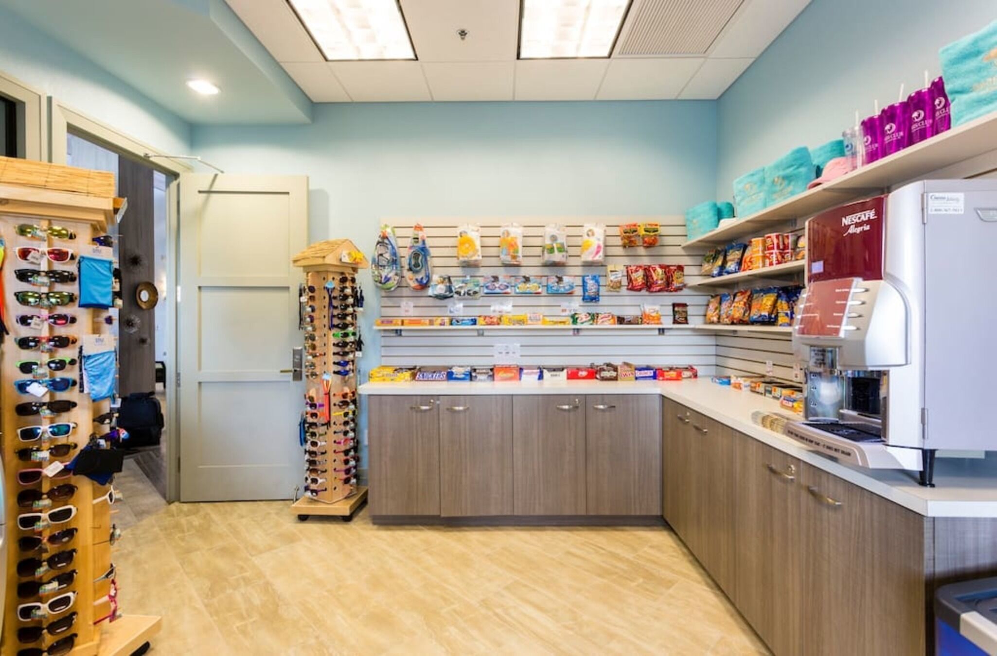 A retail store with shelves stocked with various products, a display of sunglasses, and a coffee machine.