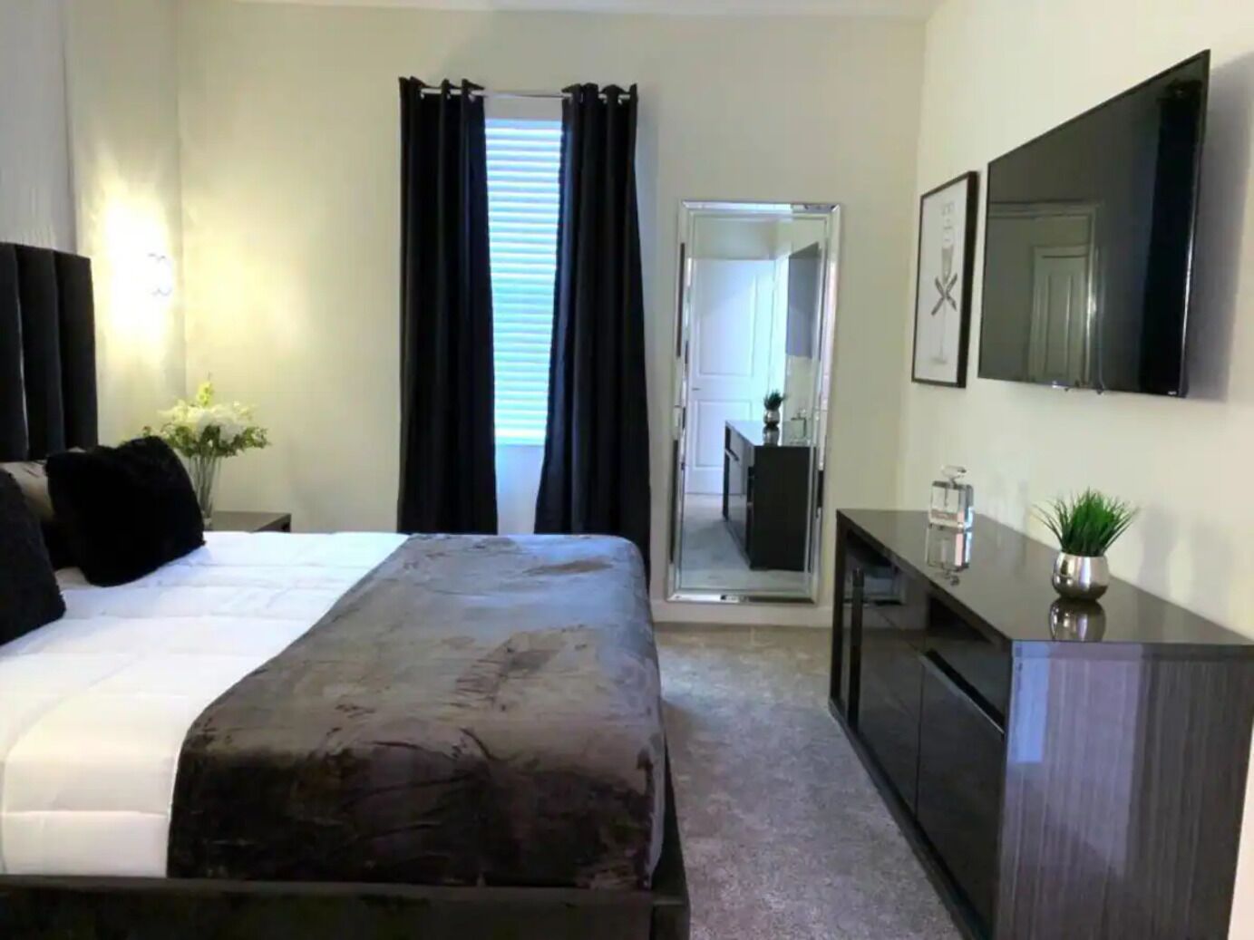 Een moderne hotelkamer met een groot bed, een nachtkastje met lamp, een dressoir en een spiegel.