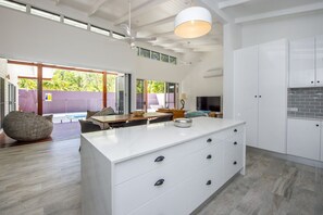 A modern kitchen with white cabinetry, a large island, and a dining area with a table and chairs. - Papillon Bleu (Horseshoe Bay)