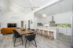 A modern kitchen with white cabinetry, a central island, and a dining area with a wooden table and black chairs. - Papillon Bleu (Horseshoe Bay)