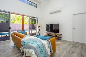 A modern living room with a sofa, TV, and a view of a pool through glass doors. - Papillon Bleu (Horseshoe Bay)