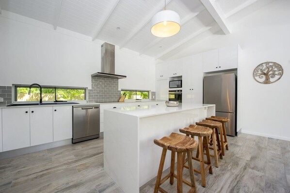 A modern kitchen with white cabinetry, a central island with stools, a stainless steel refrigerator, and a chimney. - Papillon Bleu (Horseshoe Bay)