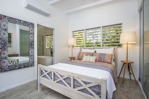 Une chambre à coucher avec un lit, des lampes de chevet, un grand miroir et une fenêtre avec des stores.