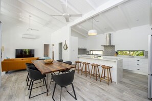 A modern kitchen with white cabinetry, a central island, and a dining area with a wooden table and black chairs. - Papillon Bleu (Horseshoe Bay)