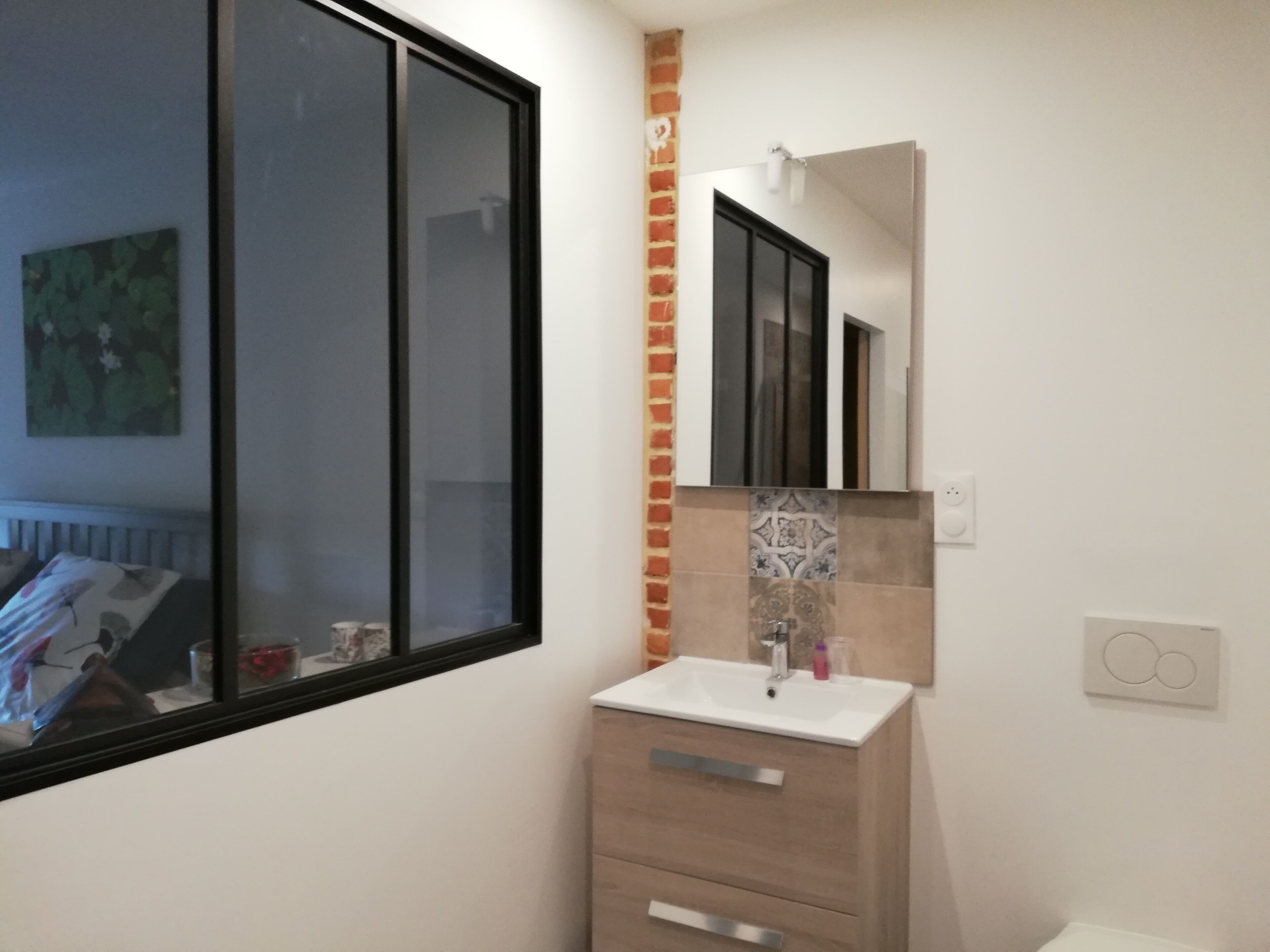 Une salle de bain avec une fenêtre, un lavabo, un miroir et un meuble.