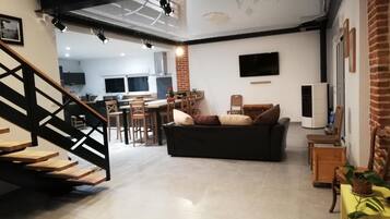 A spacious living area with a black leather sofa, wooden dining table, and a staircase with wooden steps.