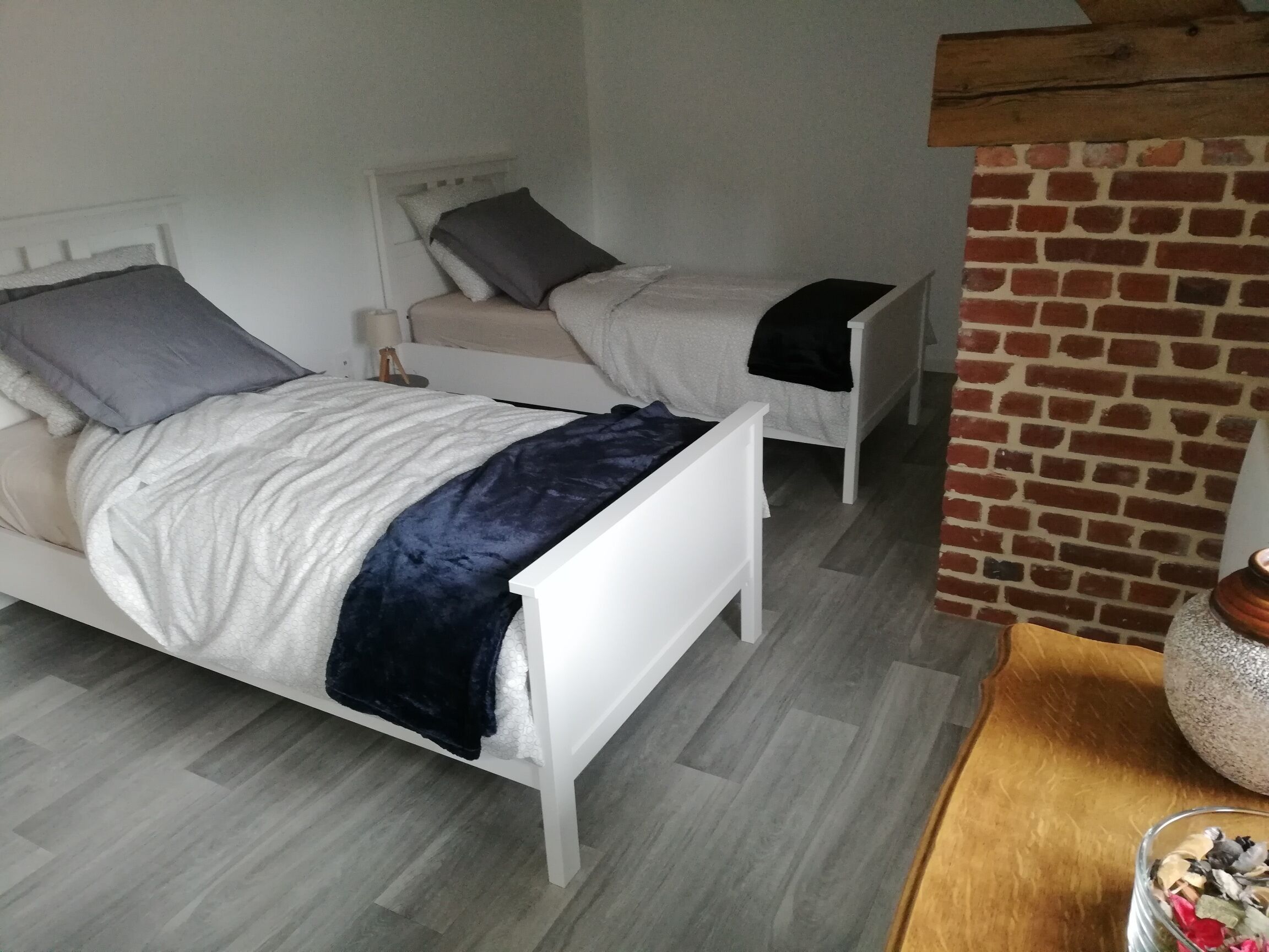 Ein Schlafzimmer mit zwei Betten, einer Ziegelwand und einem Holztisch mit einer Vase.