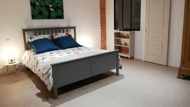 A bedroom with a bed, a nightstand, a TV, a wardrobe, and a brick wall. - La Grange du Bosquet (Honnecourt-sur-Escaut)