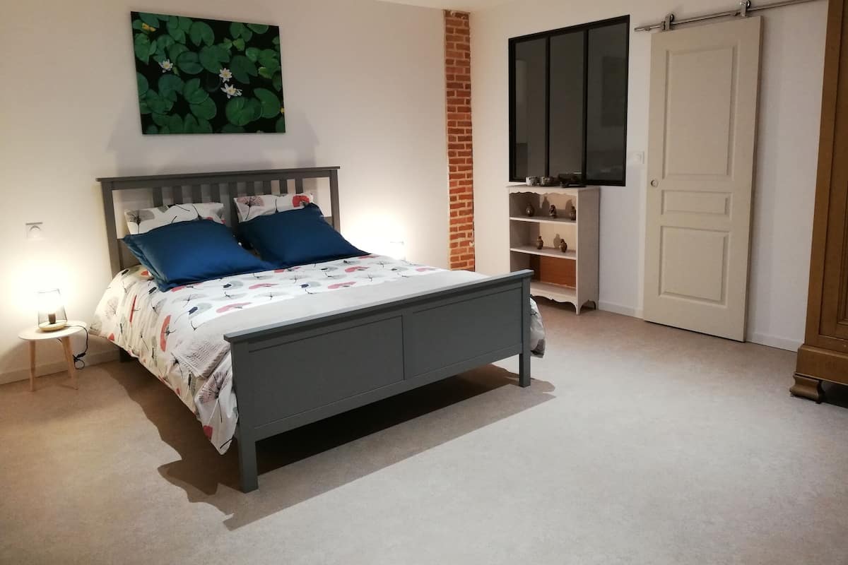 A bedroom with a bed, a nightstand, a TV, a wardrobe, and a brick wall.