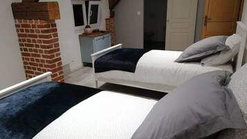 A bedroom with two beds, a brick wall, a window, and a small desk.
