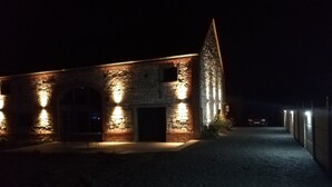 En byggnad av sten med upplysta fönster och en central dörr, omgiven av en grusgång och en låg mur.