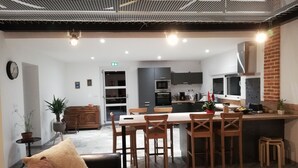 Ett modernt kök med mörka skåp, en köksö och en matplats med trästolar och en röd soffa.