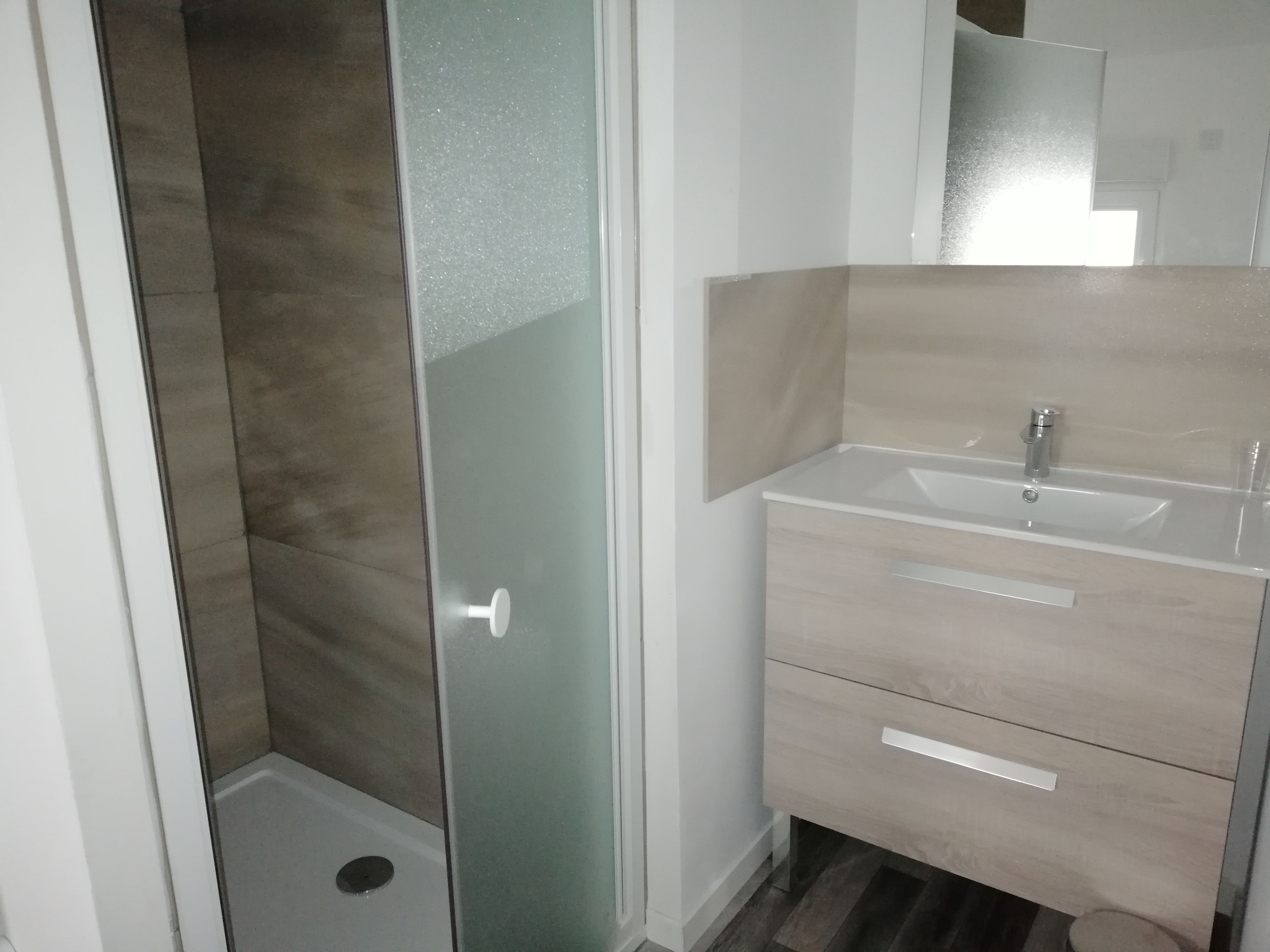 Une salle de bain avec une douche à parois de verre, un lavabo avec un miroir et un meuble-lavabo en bois doté de tiroirs.