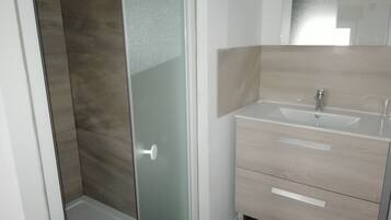 Ein Badezimmer mit Duschkabine aus Glas, Waschbecken mit Spiegel und Holzkosmetikschrank mit Schubladen.