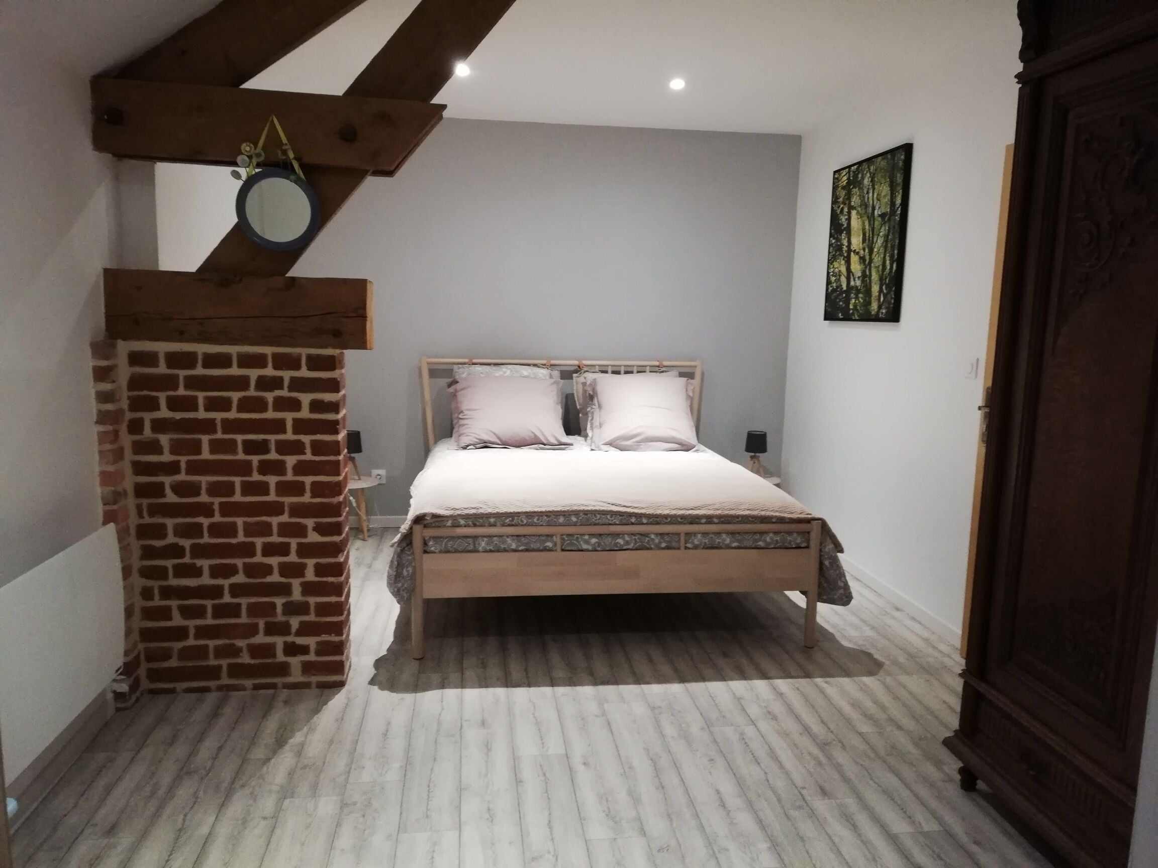 A bedroom with a wooden bed, a brick wall, and a small mirror.
