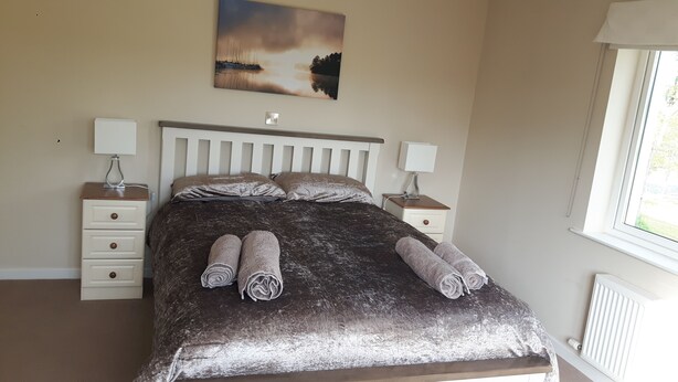 Une chambre à coucher avec un lit, deux tables de chevet, une commode, un tableau et une fenêtre.