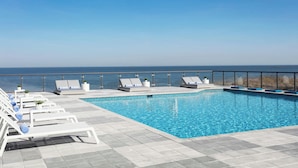Una piscina en la azotea con sillones blancos y vistas al océano.