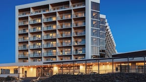 Un hotel de varios pisos con un diseño moderno, que cuenta con balcones en cada planta y un área de entrada techada.