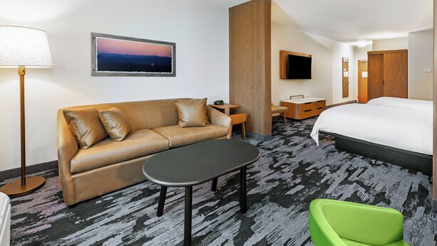 A hotel room with a sofa, a small table, a green chair, a bed, a TV, and a picture on the wall. - Fairfield Inn & Suites by Marriott Tulsa Catoosa (Catoosa)