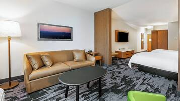 A hotel room with a sofa, a small table, a green chair, a bed, a TV, and a picture on the wall.
